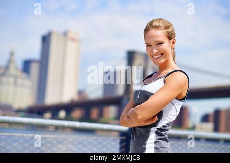Wer braucht ein Fitnessstudio? Porträt einer attraktiven jungen Frau in Sportbekleidung vor einem städtischen Hintergrund. Stockfoto