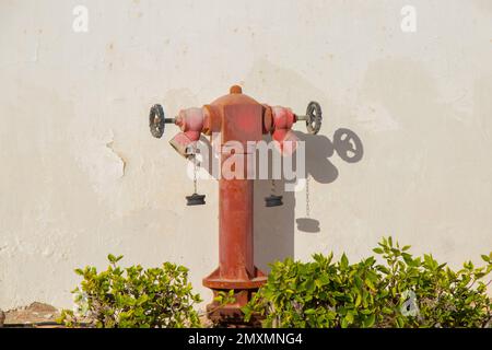 Ein alter roter Hydrant an einer weißen Wand in der Sonne Stockfoto