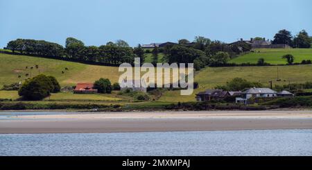 Ein Bauernhaus am grünen, hügeligen Ufer der Clonakilty Bay. Ländliche irische Landschaft. Die malerische Natur Irlands im Sommer, Haus in der Nähe von grünen Bäumen an Stockfoto