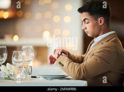 Zeitüberprüfung, Uhr und spätes Date eines Mannes am Restauranttisch allein am Valentinstag. Bokeh-Lichter, Nacht und Anzug einer Person, die auf das Abendessen wartet Stockfoto