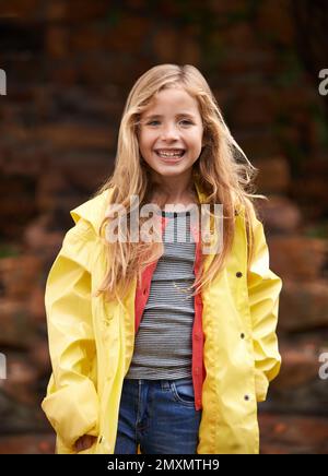 Ich lasse nicht zu, dass ein bisschen Regen meinen Spaß aufhält. Porträt eines süßen kleinen Mädchens, das einen Regenmantel trägt und draußen steht. Stockfoto