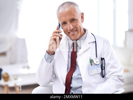 Ihre Gesundheit hat für mich oberste Priorität. Porträt eines reifen Arztes, der mit einem Handy in seiner Praxis sitzt. Stockfoto