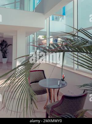 Das Innere der Hotellobby: Ein Tisch und zwei Sessel im Erholungsbereich in der Nähe des großen Fensters. Ein sonniger Tag. Stockfoto
