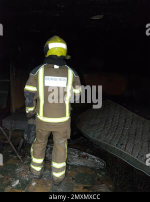 Ein Feuerwehrmann inspiziert nach einem Brand einen Raum in einem vollständig abgebrannten Haus Stockfoto