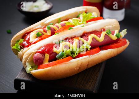 Hot Dog mit gegrillter Wurst, Tomaten und Salat auf dunklem Hintergrund. Amerikanischer Hotdog Stockfoto