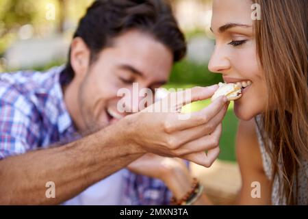 Machen Sie ein Picknick, romantisch und füttern Sie sich auf dem Rasen mit Freude, Freundlichkeit und Liebe zum Valentinstag. Mann, Frau und zusammen essen im Naturpark Stockfoto