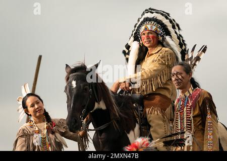 Cowboy auf seinem Pferd während der Pferderennen und im Hintergrund eine Gruppe von sechs Cowboys und Cowgirls, die den Lauf der Pferde beaufsichtigen Stockfoto