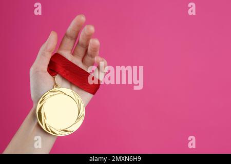 Frau mit Goldmedaille auf pinkfarbenem Hintergrund, Nahaufnahme. Raum für Design Stockfoto