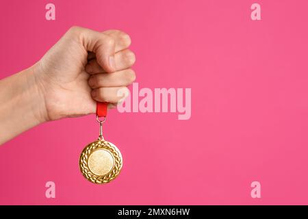 Frau mit Goldmedaille auf pinkfarbenem Hintergrund, Nahaufnahme. Raum für Design Stockfoto