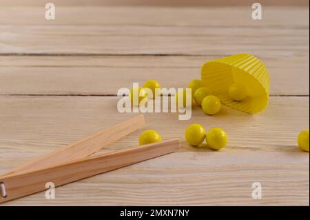Gelbe Kugeln und Holzpinzette zur Entwicklung der Feinmotorik bei Kindern. Auf einem Holzhintergrund. Stockfoto