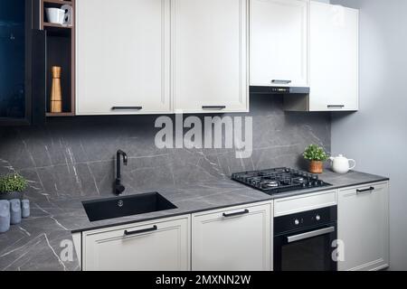 Innenausstattung der weiß-grauen Küche, horizontale, lineare Anordnung. Luxuriöse, modern ausgestattete Küche in flachem Design mit Glaselementen. Stockfoto