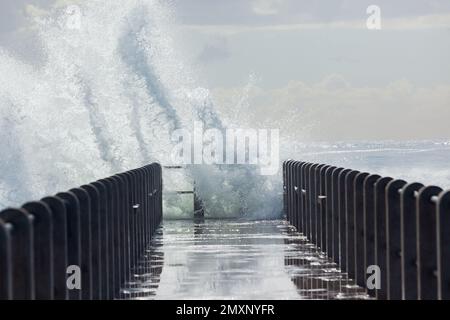 Wellenenergie Wasser explodierte vor der Strandpier-Anlegestelle Wanderweg Plattform. Stockfoto
