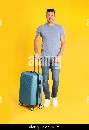 Ein hübscher Mann mit Koffer für die Sommerreise auf gelbem Hintergrund. Urlaubsreisen Stockfoto