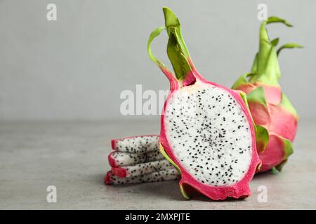 Köstliche geschnittene und ganze Drachenfrüchte (Pitahaya) auf einem grauen Tisch. Platz für Text Stockfoto