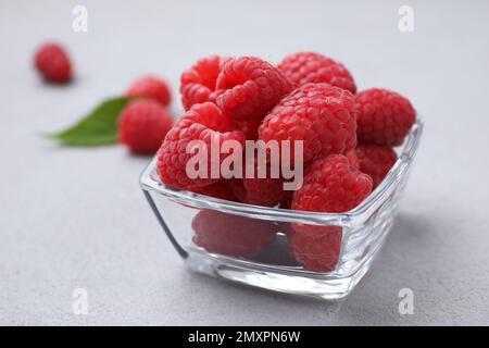 Köstliche frische, reife Himbeeren in einer Glasschüssel auf einem grauen Tisch, Nahaufnahme Stockfoto