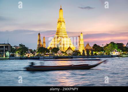 Die Boote bewegen sich in der Dämmerung entlang des Flusses, vor dem wunderschönen goldbeleuchteten Tempel der Morgendämmerung, goldenes Licht, das von der Wasseroberfläche reflektiert wird, Stockfoto