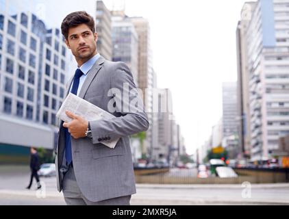 Ein Mann über die Stadt. Ein gutaussehender junger Geschäftsmann mit einer Zeitung, der in der Stadt herumläuft. Stockfoto
