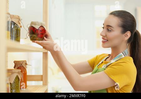 Frau, die eingelegte Gemüsegläser drinnen in Regale stellt Stockfoto