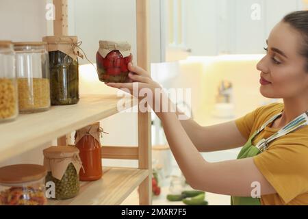 Frau, die eingelegte Gemüsegläser drinnen in Regale stellt Stockfoto