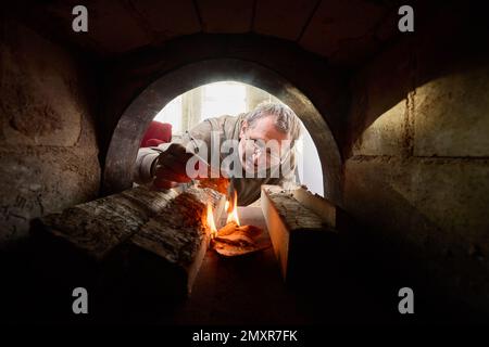 Ein Mann mittleren Alters macht Feuer in einem Steinofen. Stockfoto