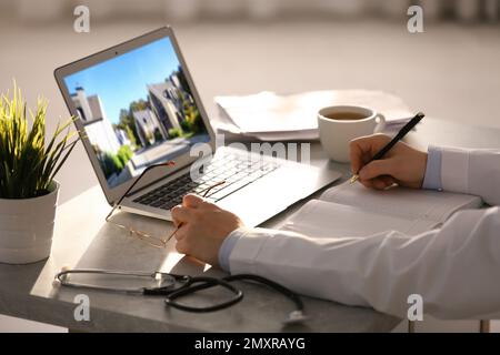 Online-Service für Immobilienmakler. Ein Arzt wählt ein neues Haus über Laptop, Nahaufnahme Stockfoto
