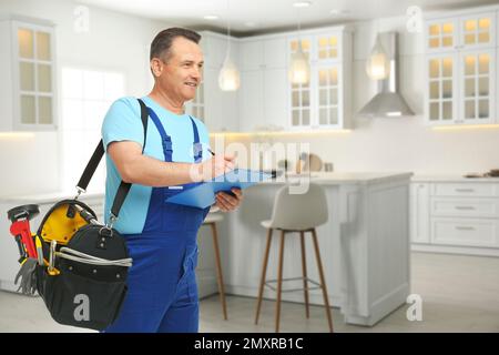 Reifer Klempner mit Klemmbrett und Werkzeugtasche in der Küche, Platz für Text Stockfoto