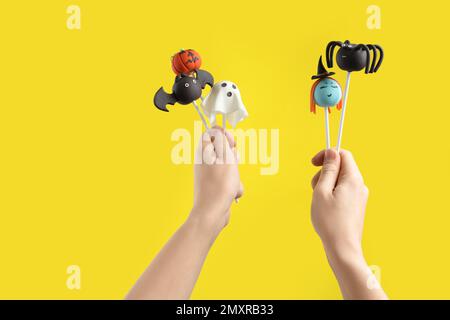 Eine Frau mit leckerem Kuchen auf gelbem Hintergrund, Nahaufnahme. Halloween-Feier Stockfoto