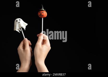 Frau mit leckeren Kuchenwürfeln und Platz für Text auf schwarzem Hintergrund, Nahaufnahme. Halloween-Feier Stockfoto