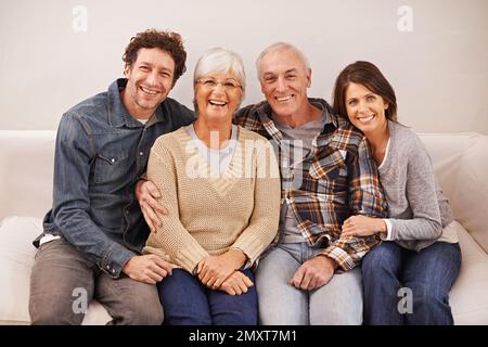 Ich Besuche die Schwiegereltern. Ein Porträt glücklicher reifer Eltern, die mit ihren erwachsenen Kindern zu Hause sitzen. Stockfoto