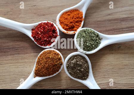 Verschiedene Gewürze auf Holzhintergrund isoliert. Gemahlener schwarzer Pfeffer, Chilipulver, Cayennepfeffer, Minzpulver, cajun-Würzmittel. Stockfoto