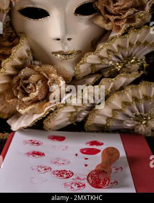 Ein Stempel mit der Figur einer Katze wird auf einem weißen Tuch mit roter Tinte und einer Karnevalsmaske im Hintergrund verwendet Stockfoto