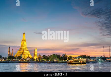 In der Dämmerung gleitet die Silhouette eines thailändischen Langschwanzboots vorbei an den goldenen Pagoden der Tempelanlage, während sie auf den klaren Sonnenuntergang zeigen Stockfoto