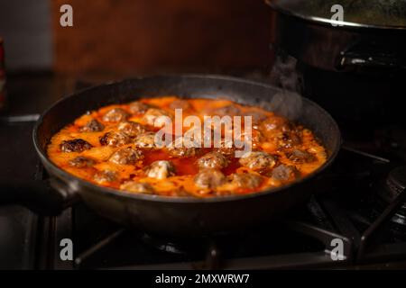 Hausgemachte Fleischbällchen in einer Pfanne in einer Sauce aus Tomaten und saurer Sahne zubereiten. Stockfoto