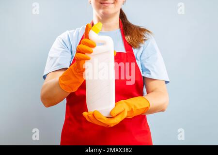 Frau im Handschuh, die eine Plastikflasche mit Reinigungsmittel auf blauem Hintergrund hält Stockfoto