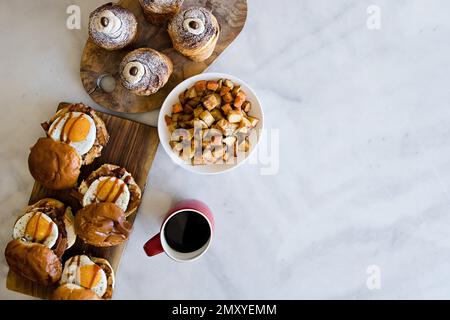 Ein Blick von oben auf Gourmet-Eier-Sandwiches und Gebäck auf Holzbrettern auf einem weißen Tisch mit Kaffee Stockfoto