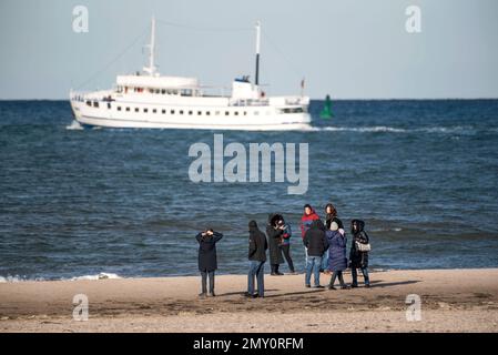 04. Februar 2023, Mecklenburg-Vorpommern, Warnemünde: Kinderwagen gehen unter blauem Himmel und Sonnenschein am Strand von Warnemünde, im Hintergrund ein Passagierschiff an der Ostsee. Die Winterferien beginnen an diesem Wochenende in Mecklenburg-Vorpommern. Foto: Frank Hormann/dpa - ACHTUNG: Nur im Vollformat verwenden Stockfoto