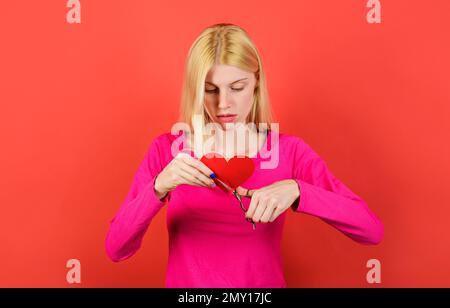 Trauriges Mädchen schneidet rotes Herz mit einer Schere. Paare divergieren. Beziehungen brechen, Streit und Scheidung. Stockfoto