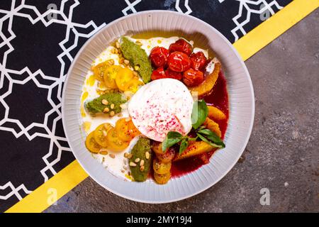 Salat mit Buratta-Käse und Tomaten mit Pesto-Sauce in einer Schüssel mit Blick von oben Stockfoto