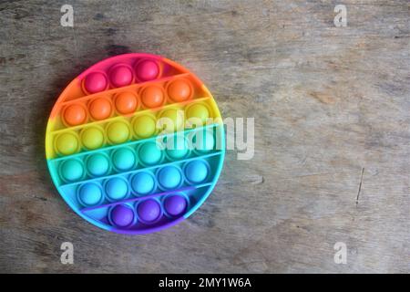 Regenbogenfarbenes Silikon Pop IT Kinderspielzeug mit Holzstruktur Stockfoto