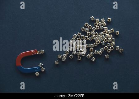 Hufeisenmagnet mit einem Haufen Metallalphabet auf schwarzem Hintergrund. Stockfoto