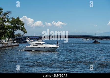 Ein weißes Schnellboot, das auf dem blauen Wasser der Guanabara-Bucht, dem nahe gelegenen Sao Bento Pier und der Arnaldo Luz-Brücke unter dem klaren blauen Himmel am Sommernachmittag segelt. Stockfoto