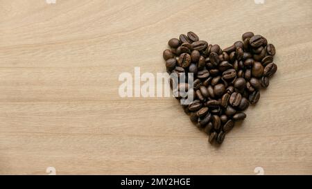 Kaffeebohnen in Herzform auf Holzhintergrund mit Kopierbereich. Stockfoto