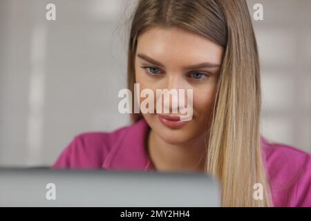 Porträt einer wunderschönen blonden Frau, die zu Hause am Computer arbeitet. Nahaufnahme einer hübschen Frau in 20s, die zu Hause ein Notebook benutzt Stockfoto