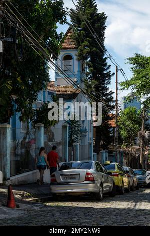 Autos in einer Reihe auf der Kopfsteinpflasterstraße Ladeira de Santa Teresa im Viertel Santa Teresa unter dem sonnigen blauen Himmel am Sommernachmittag geparkt. Stockfoto