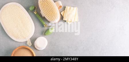 Badeprodukte, trockener Lehm, Massagebürste und Jadewalze auf grauem Steinhintergrund. Flach liegend, Banner, Kopierraum. Stockfoto