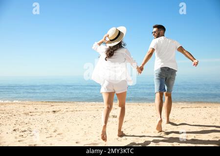 Ein junges Paar, das am Strand in der Nähe des Meeres rennt. Hochzeitsreise Stockfoto