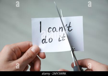 Eine Frau schneidet Papier mit Text, ich kann es nicht auf unscharfem Hintergrund machen, Nahaufnahme Stockfoto