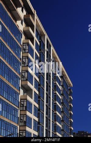 Architektonisches Fragment der Fassade eines Apartmentgebäudes, Backsteinwände und Glasbalkone vor dem blauen Himmel Stockfoto
