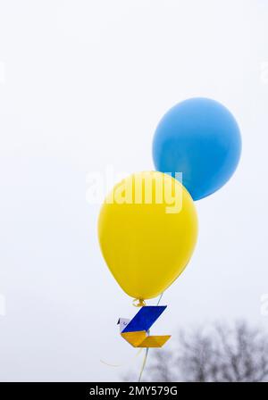 Papiertaube des Friedens, fliegt in den Himmel auf zwei gelbblauen Ballons der ukrainischen Flagge. Unterstützt Die Ukraine. Stoppt den Krieg. Symbol des Friedens und des Glaubens an Stockfoto