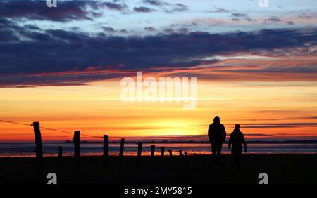 Husum, Deutschland. 04. Februar 2023. Zwei Personen laufen kurz nach Sonnenuntergang an der Nordsee nahe Husum vor einem bunten Himmel. Kredit: Christian Charisius/dpa/Alamy Live News Stockfoto